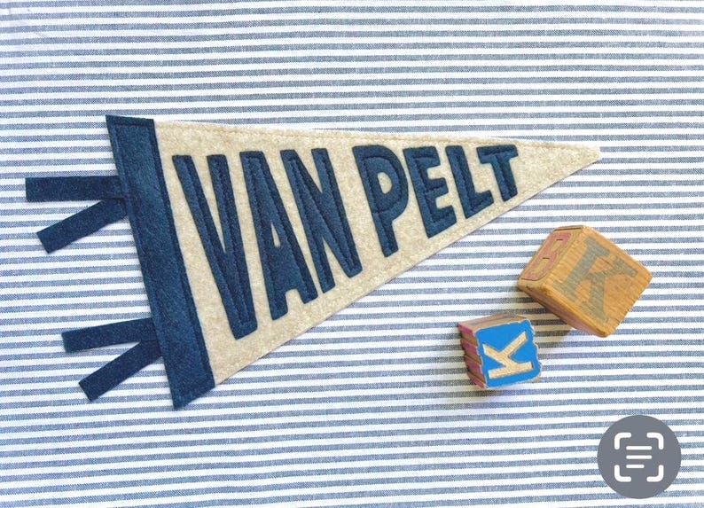 Peut inclure: Une banni&egrave;re en feutre beige avec le nom "VAN PELT" en lettres bleu marine. La banni&egrave;re a une bordure et des attaches bleu marine. Deux blocs de lettres en bois sont &agrave; c&ocirc;t&eacute; de la banni&egrave;re, dont un avec la lettre "K". Le fond est un tissu &agrave; rayures bleues et blanches.