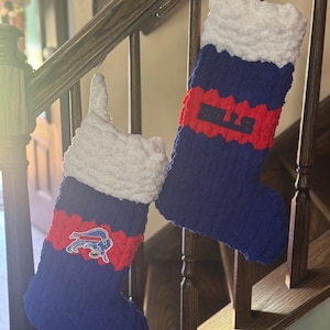 May include: Two handmade Christmas stockings. The stockings are blue with a red band and white cuff. One stocking has the word "BILLS" in red, and the other has a Buffalo Bills logo.