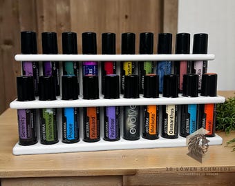 May include: A white, tiered essential oil display rack holding numerous essential oil bottles with black caps. The bottles are labelled with various names and colours. The rack is made of white material and sits on a wooden surface.