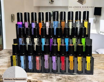 May include: A black wooden stand with 24 clear glass roller bottles filled with essential oils. The bottles are labeled with names like "ZenGest", "Serenity", "Rose", and "Helichrysum". The stand is on a wooden surface. The text "Weitere Farbauswahl" is visible on the stand.