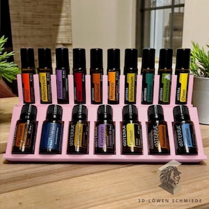 Op de afbeelding: Een roze houten rek met 18 kleine glazen flesjes met etherische oliën. De flesjes zijn gelabeld met de merknaam "dōTERRA" en de namen van de oliën, zoals "On Guard", "Neroli", "Helichrysum", "Serenity", "Rose", "Motivate", "Lemon", "Lavender", "Frankincense", "Shinrin-Yoku", "Cheer" en "ZenGest".