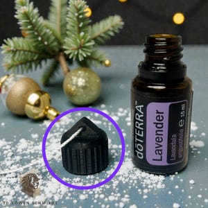 Puede incluir: Un tapón de botella negro y geométrico con una cuerda blanca adjunta. El tapón está junto a una botella de aceite esencial de lavanda y adornos navideños. La etiqueta de la botella dice "Lavender".