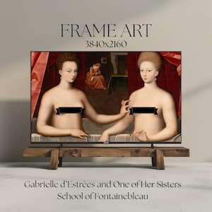 Op de afbeelding: Een ingelijste kunstdruk van het schilderij "Gabrielle d'Estrées en een van haar zusters" van de School van Fontainebleau. Het kunstwerk toont twee vrouwen in een bad, met een rode gordijnachtergrond. Het frame wordt weergegeven op een rustieke houten standaard.
