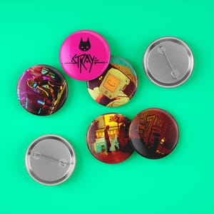May include: A set of seven round pins with various designs. The pins feature images from the video game Stray, including a cat, a robot, and a city scene. The pins are silver with a black and white design.