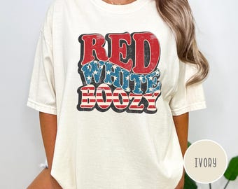 May include: Ivory-colored t-shirt with the words "RED WHITE BOOZY" in a retro font. The text features red, white, and blue colors, with stars and stripes designs. The shirt has a relaxed fit and short sleeves.