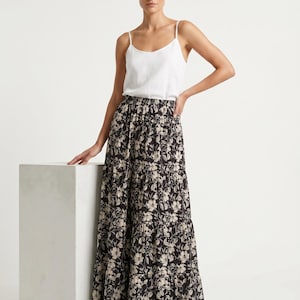 Può includere: Un top a canotta bianco abbinato a una gonna lunga a balze con sfondo nero e un motivo floreale color crema e beige. La gonna ha un elastico in vita. L'outfit è adatto per abbigliamento casual.