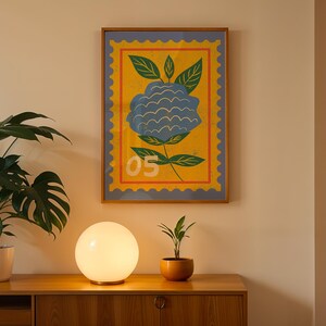 Puede incluir: Una impresi&oacute;n art&iacute;stica enmarcada con una ilustraci&oacute;n de una flor azul sobre un fondo amarillo, con un dise&ntilde;o de sello postal. Se exhibe sobre un mueble de madera con una l&aacute;mpara esf&eacute;rica y plantas en macetas.