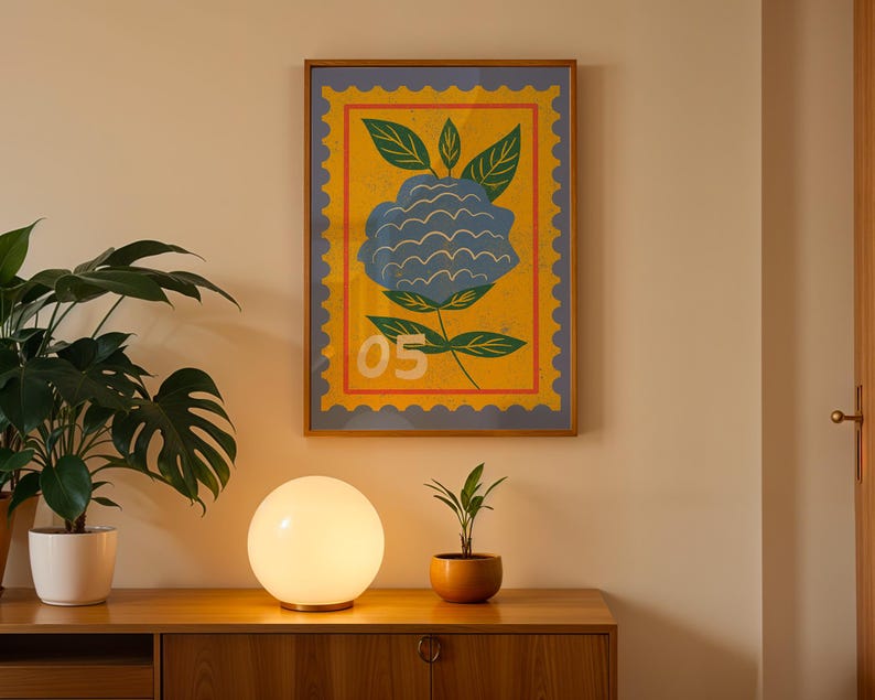 Puede incluir: Una impresi&oacute;n art&iacute;stica enmarcada con una ilustraci&oacute;n de una flor azul sobre un fondo amarillo, con un dise&ntilde;o de sello postal. Se exhibe sobre un mueble de madera con una l&aacute;mpara esf&eacute;rica y plantas en macetas.
