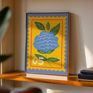 Puede incluir: Impresi&oacute;n art&iacute;stica enmarcada con una flor azul estilizada sobre fondo amarillo, similar a un sello postal. El dise&ntilde;o incluye hojas verdes y el n&uacute;mero "05" en blanco. La impresi&oacute;n enmarcada se exhibe en una estanter&iacute;a de madera.