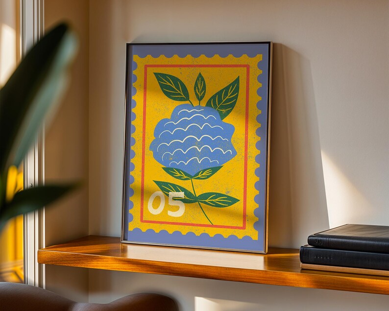 Puede incluir: Impresi&oacute;n art&iacute;stica enmarcada con una flor azul estilizada sobre fondo amarillo, similar a un sello postal. El dise&ntilde;o incluye hojas verdes y el n&uacute;mero "05" en blanco. La impresi&oacute;n enmarcada se exhibe en una estanter&iacute;a de madera.