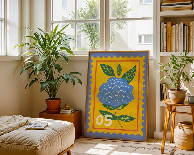 Puede incluir: Una impresi&oacute;n art&iacute;stica enmarcada con una ilustraci&oacute;n de una flor azul sobre un fondo amarillo y un borde azul. La obra de arte incluye hojas verdes y el n&uacute;mero "05". La impresi&oacute;n se exhibe en una habitaci&oacute;n con plantas y una ventana.