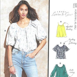 May include: McCall's sewing pattern M8256 features a woman wearing a floral print top and jeans. The pattern includes illustrations of different top styles, including a yellow top, a patterned top, and a green top. The text "Learn to Sew" is also visible.