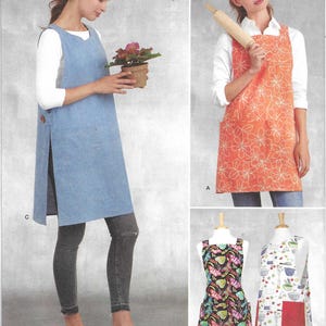 May include: Simplicity sewing pattern S9409 featuring four apron designs. View A is an orange floral apron, B is a black butterfly print apron, C is a solid blue side-buttoned tunic apron, and D is a white apron with kitchen utensil graphics.