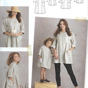 May include: Simplicity sewing pattern S8856 A, featuring "The Artisan Dress." The image shows a woman and child wearing the dress, along with line drawings of the dress design. The dress is a loose-fitting style with pockets.