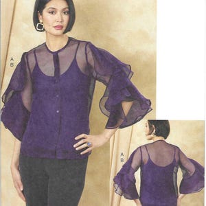 May include: Vogue Patterns sewing pattern featuring a woman wearing a purple blouse with sheer, ruffled sleeves over a matching camisole. The pattern includes sizes N5 (10-12-14-16-18). The Vogue Patterns logo is visible.