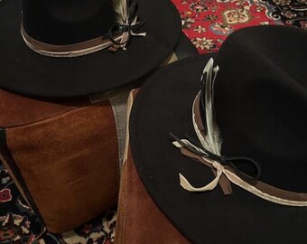 May include: Two black felt fedora hats with brown and white feather accents and a brown ribbon band.