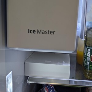 May include: A close-up of the interior of a refrigerator. The image shows the "Ice Master" ice maker and a white ice storage bin. A bag of chips is visible in the bottom of the refrigerator.