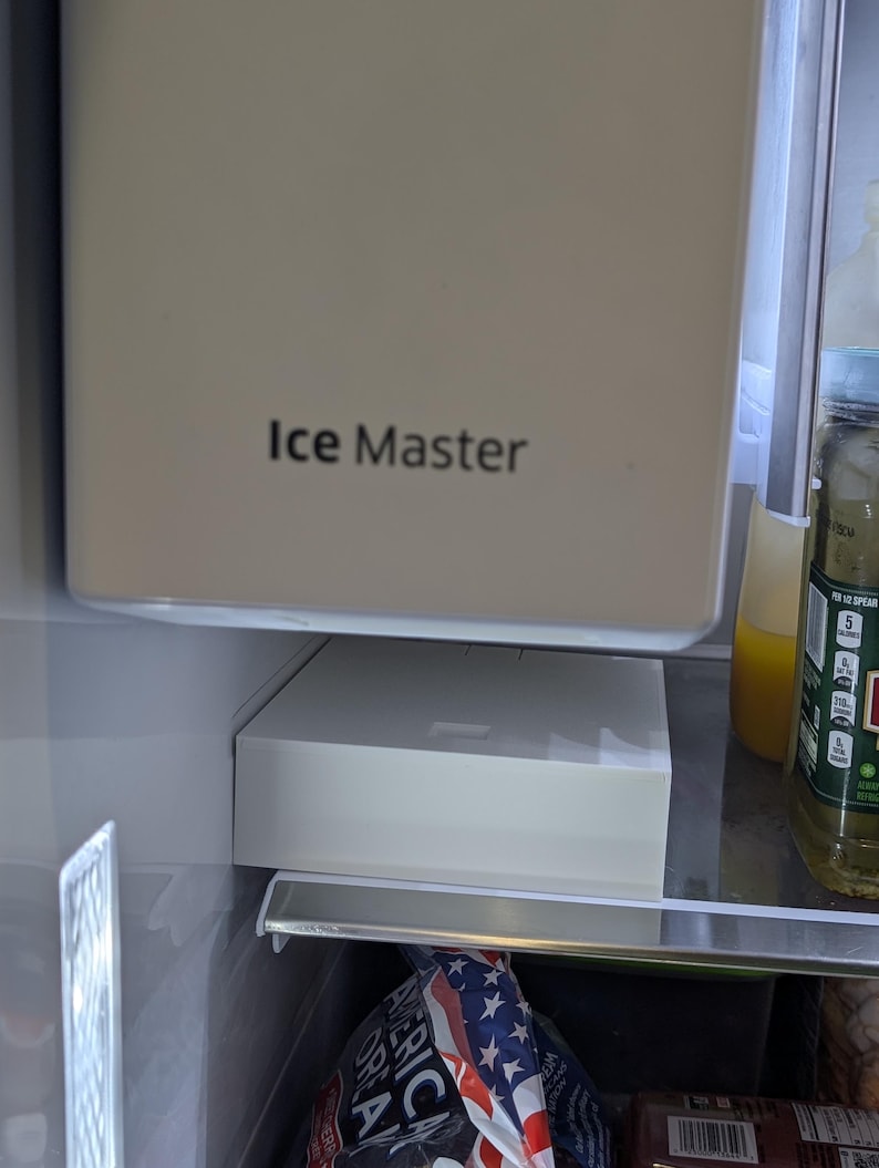 May include: A close-up of the interior of a refrigerator. The image shows the "Ice Master" ice maker and a white ice storage bin. A bag of chips is visible in the bottom of the refrigerator.
