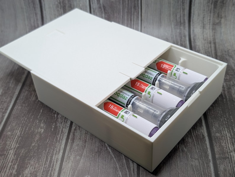 May include: A white rectangular box with a hinged lid, partially open to reveal several cylindrical items. The items are white with red and green accents, and the number "15" is visible on each. The box is on a wooden surface.