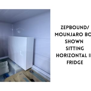 May include: A white rectangular box with a small square indentation is positioned horizontally inside a refrigerator. The text on the right side of the image reads: ZEPBOUND/MOUNJARO BOX SHOWN SITTING HORIZONTAL IN FRIDGE.