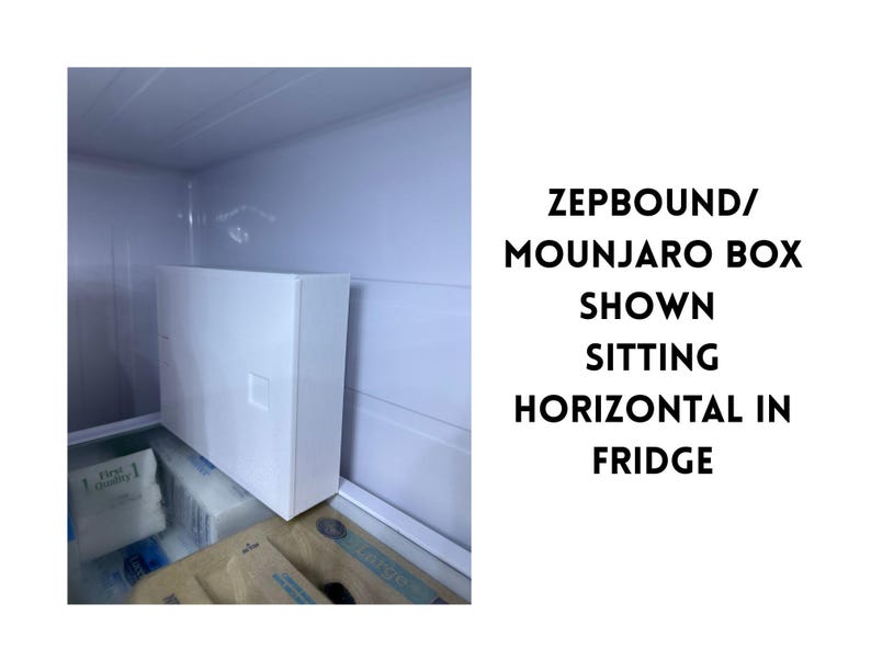 May include: A white rectangular box with a small square indentation is positioned horizontally inside a refrigerator. The text on the right side of the image reads: ZEPBOUND/MOUNJARO BOX SHOWN SITTING HORIZONTAL IN FRIDGE.