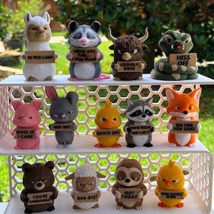May include: A collection of whimsical animal figurines, each holding a sign with a humorous phrase. The figurines include a llama, raccoon, bull, snake, pig, rabbit, duck, raccoon, fox, bear, sheep, sloth, and chick.