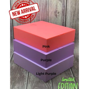 May include: A stack of three rectangular boxes in shades of pink, purple, and light purple. The top box is pink, the middle box is purple, and the bottom box is light purple. The boxes have the words "Pink", "Purple", and "Light Purple" printed on them.