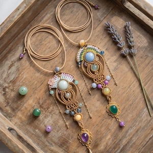 May include: Two macrame necklaces featuring tan cord, intricate woven patterns, and various gemstones including light blue, green, yellow, and purple cabochons. Each pendant includes small metal accents, dangling beads, and a long adjustable cord.
