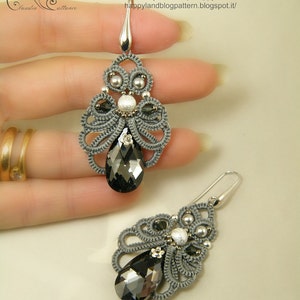 May include: A pair of gray and silver earrings with teardrop-shaped black crystals. The earrings are made with a delicate, intricate design and feature small silver beads and a silver flower accent.