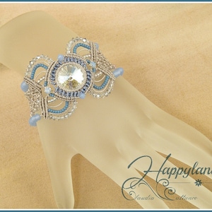 Könnte beinhalten: Ein silbernes und blaues Perlenarmband mit einem großen, klaren Kristall in der Mitte. Das Armband liegt auf einer hellbraunen Oberfläche.