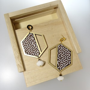May include: A pair of gold geometric earrings with a brown and white patterned design. The earrings have a dangling white bead at the bottom.