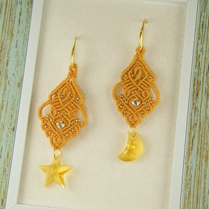 May include: A pair of gold-toned earrings with a delicate, intricate design. Each earring features a dangling charm, one a star and the other a crescent moon.
