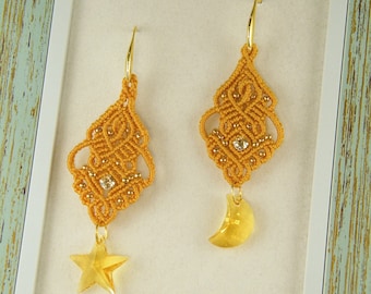 Pode incluir: Um par de brincos dourados com um design delicado e intrincado. Cada brinco tem um charme pendurado, um uma estrela e o outro uma lua crescente.