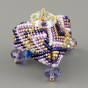 May include: A small, square, beaded box with a crystal top and gold accents. The box is decorated with purple, white, and gold beads and has four crystal feet.