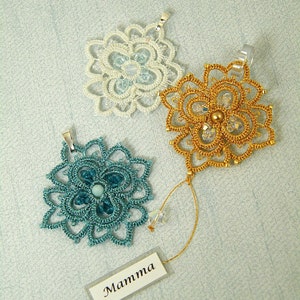 May include: Three crocheted flower pendants with different colored beads. The pendants are on a light blue background. The tag reads "Mamma".