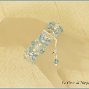 May include: A light blue bracelet with silver accents and blue crystals. The bracelet is made with a knotted cord and has a dangling charm.