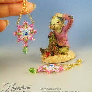 May include: A pair of pink and green beaded earrings with a star-shaped design. The earrings are hanging from gold chains.