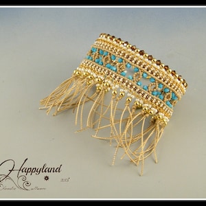 May include: A gold and turquoise beaded bracelet with a fringe of brown string. The bracelet is made with small beads and has a delicate design.