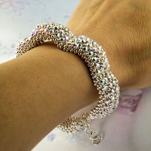 May include: A silver beaded bracelet with a wavy design. The bracelet is made with small, iridescent beads and has a silver clasp.