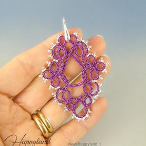 May include: Purple and silver beaded teardrop-shaped earrings with a silver hook closure. The earrings are held in a hand.