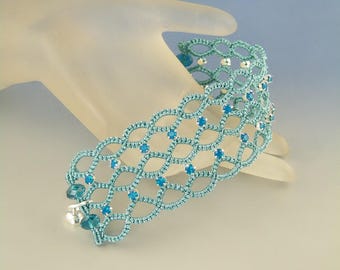 Könnte beinhalten: Ein türkisfarbenes gehäkeltes Armband mit silbernen Perlen und blauen Kristallen. Das Armband befindet sich auf einer weißen Mannequin-Hand.