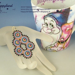 Op de afbeelding: Een paar blauwe en gouden kralen oorbellen met een cirkelvormig ontwerp. De oorbellen hangen aan een witte mannequinhand.