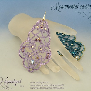 Può includere: Un paio di orecchini ornati color lavanda, con un design floreale in pizzo, impreziositi da cristalli scintillanti. Gli orecchini sono esposti su una mano traslucida. Il testo "Monumental earrings" è visibile.