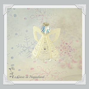 May include: White beaded angel ornament with iridescent glass wings and a beaded halo. The angel is hanging from a white string against a background of white snowflakes.