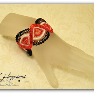 Peut inclure: Un bracelet en perles rouge, blanc et noir avec un motif géométrique. Le bracelet est sur une main de mannequin blanche.