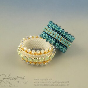May include: Two beaded bracelets. One is white with gold and iridescent accents. The other is turquoise and teal with gold accents. The bracelets are handmade and feature intricate beadwork. The background is a gradient of light blue and gray.