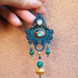Puede incluir: Pendiente de macramé azul turquesa y dorado con una piedra de labradorita, una piedra blanca y cuentas verdes.
