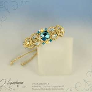 May include: A gold and teal blue macrame bracelet with a large teal blue crystal in the centre. The bracelet is tied with a knot and has gold beads and small teal blue crystals.
