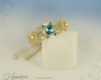 May include: A gold and teal blue macrame bracelet with a large teal blue crystal in the center. The bracelet is tied with a knot and has gold beads and small teal blue crystals.
