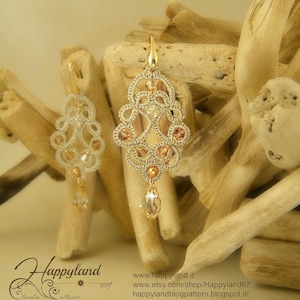 May include: A pair of gold-tone earrings with a delicate, intricate design. The earrings are made of a fine, woven wire and feature small, clear crystals. The earrings are hanging from a wooden surface.